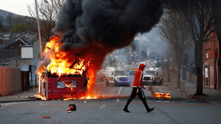 A man walks past a hijacked bus burning on The Shankill Road as protests continue in Belfast, Northern Ireland, April 7, 2021.