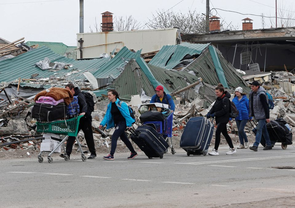 Local residents carry belongings past a destroyed building in Mariupol