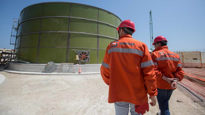 Workers walk past a gas storage tank at the constriction site of the Trans Adriatic Pipeline receiving terminal in Melendugno, Italy, on Tuesday, May 22, 2018.