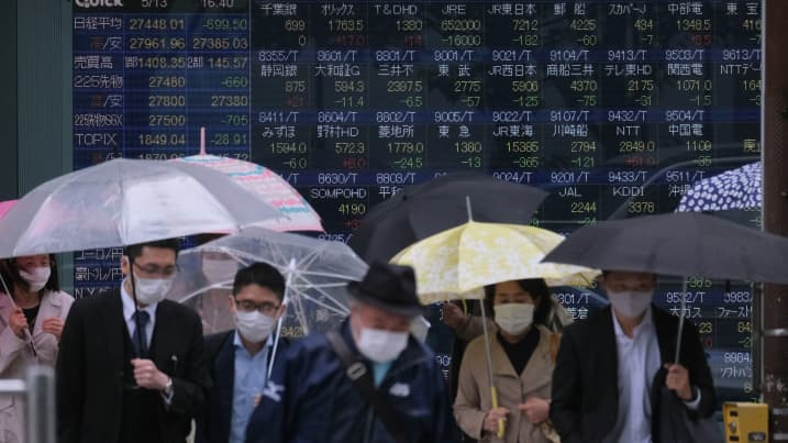 Pedestrians cross a road in front of an electronic quotation board displaying the numbers of company stock prices on the Tokyo Stock Exchange in Tokyo on May 13, 2021.