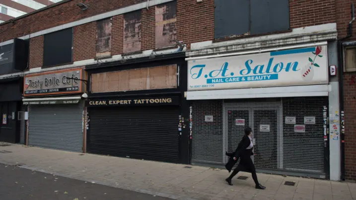 A woman walks past rundown, shuttered shops in Romford, England.